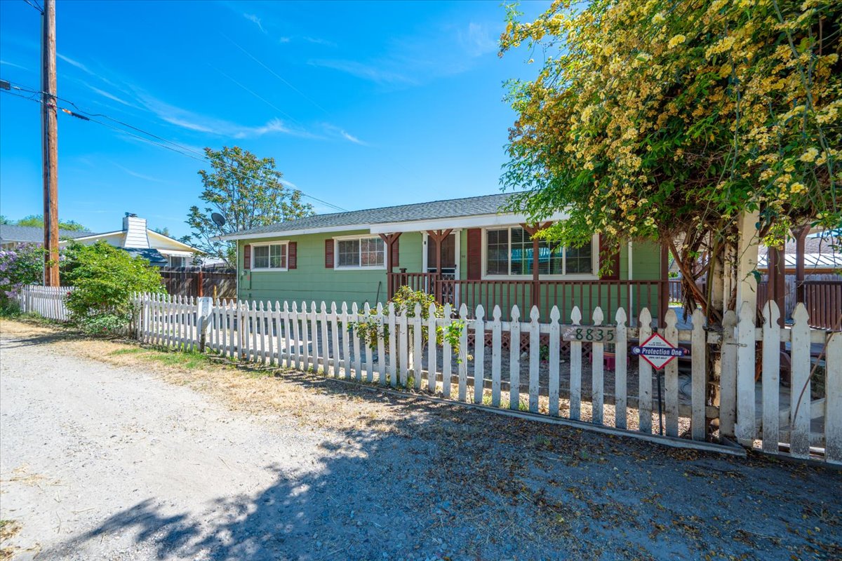 Front of 8835 Kennedy Lane, a single-story green home with a covered porch and white picket fence in San Miguel, CA